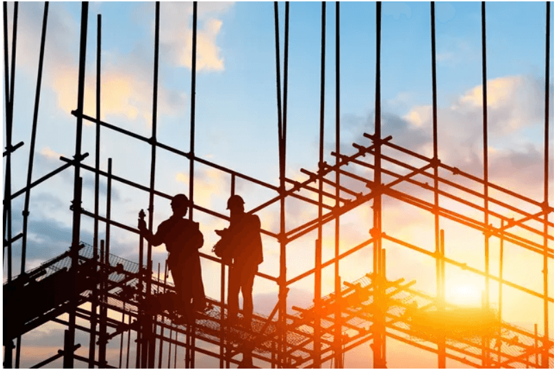 Construction workers on scaffolding at sunset.