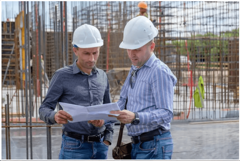 Construction workers reviewing blueprints at site.