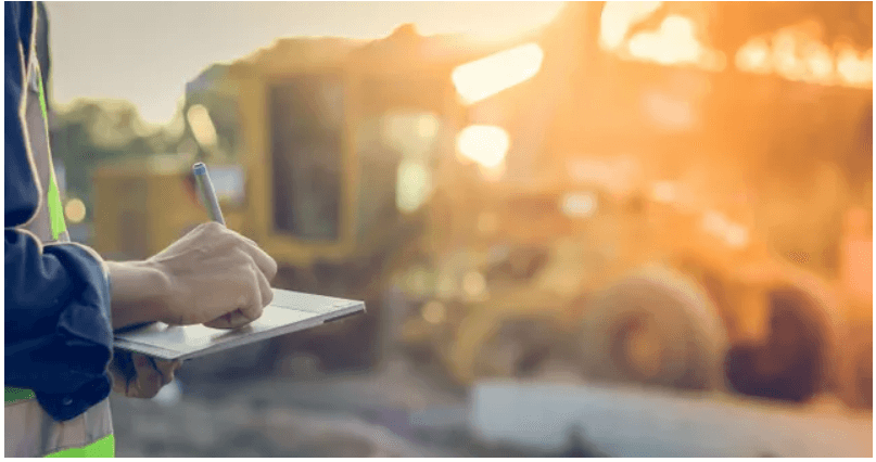 Person writing on clipboard at construction site.